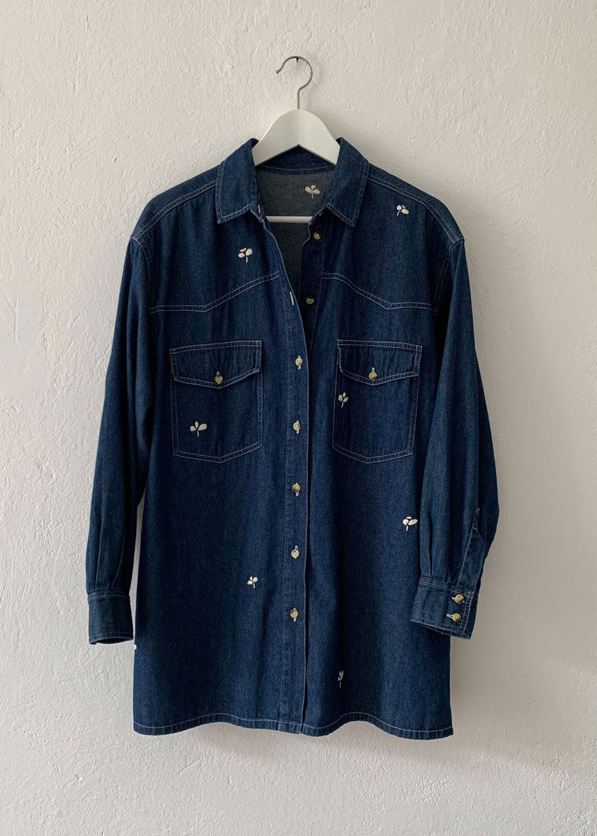 denim shirt with small hand embroidered flowers hanging on hanger