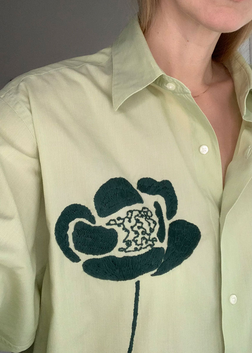Close-up of hand embroidered green flower. Worn by a person. 